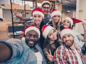 Self portrait of mixed race friends : african, american, asian, caucasian, young smiling bearded men and beautiful women in red christmas hat showing peace symbol to the camera, celebrating new year in the office