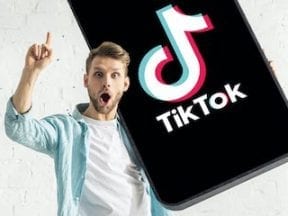 Photo of a young male holding a smartphone with TikTok app on it