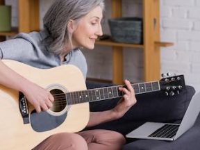 Lady playing guitar while reading lessons on a computer