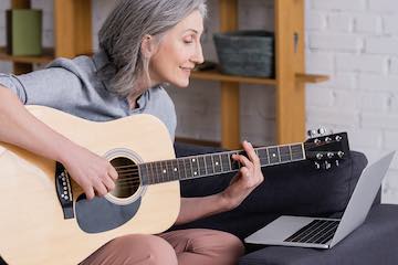 Lady playing guitar while reading lessons on a computer