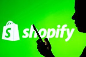 Shopify logo in the background of a silhouetted woman holding a mobile phone.