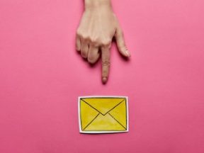 Image of a hand pointing to yellow mail sign on a pink background.