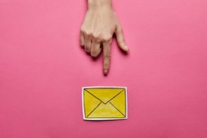 Image of a hand pointing to yellow mail sign on a pink background.