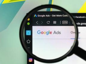 Google Ads application icon on Apple iMac monitor screen under magnifying glass.