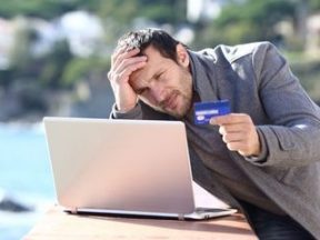 Photo of a man looking frustrated with a credit card and computer