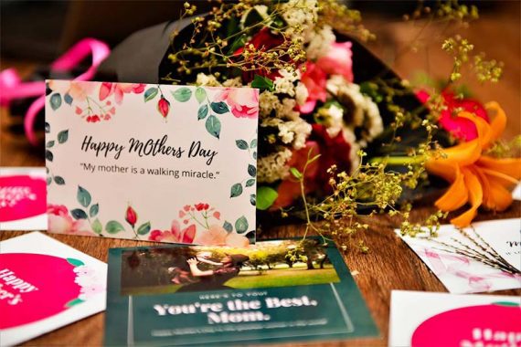 Bir masada Anneler Günü çiçeklerinin ve hediye kartlarının resmi.