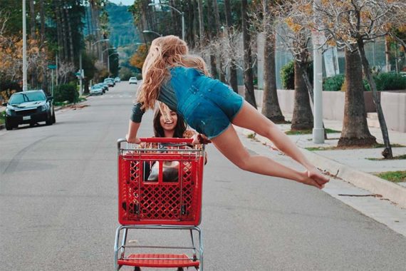 Imagen de dos niñas riéndose empujando un carrito de compras por la calle