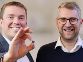 Photo of two men, one holding a small hearing aid