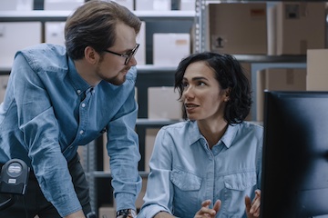 Photo of a male and female in a warehouse looking at a computer