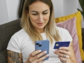 Photo of a female looking at a smartphone while holding a credit card