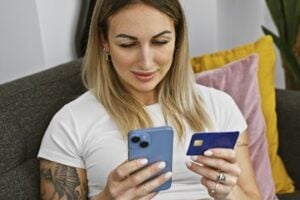 Photo of a female looking at a smartphone while holding a credit card