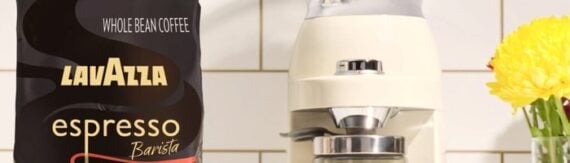 Bag of Lavazza Espresso Barista whole bean coffee beside a cream-colored espresso machine on a tiled kitchen counter. Bag of Lavazza Espresso Barista whole bean coffee beside a cream-colored espresso machine on a tiled kitchen counter.
